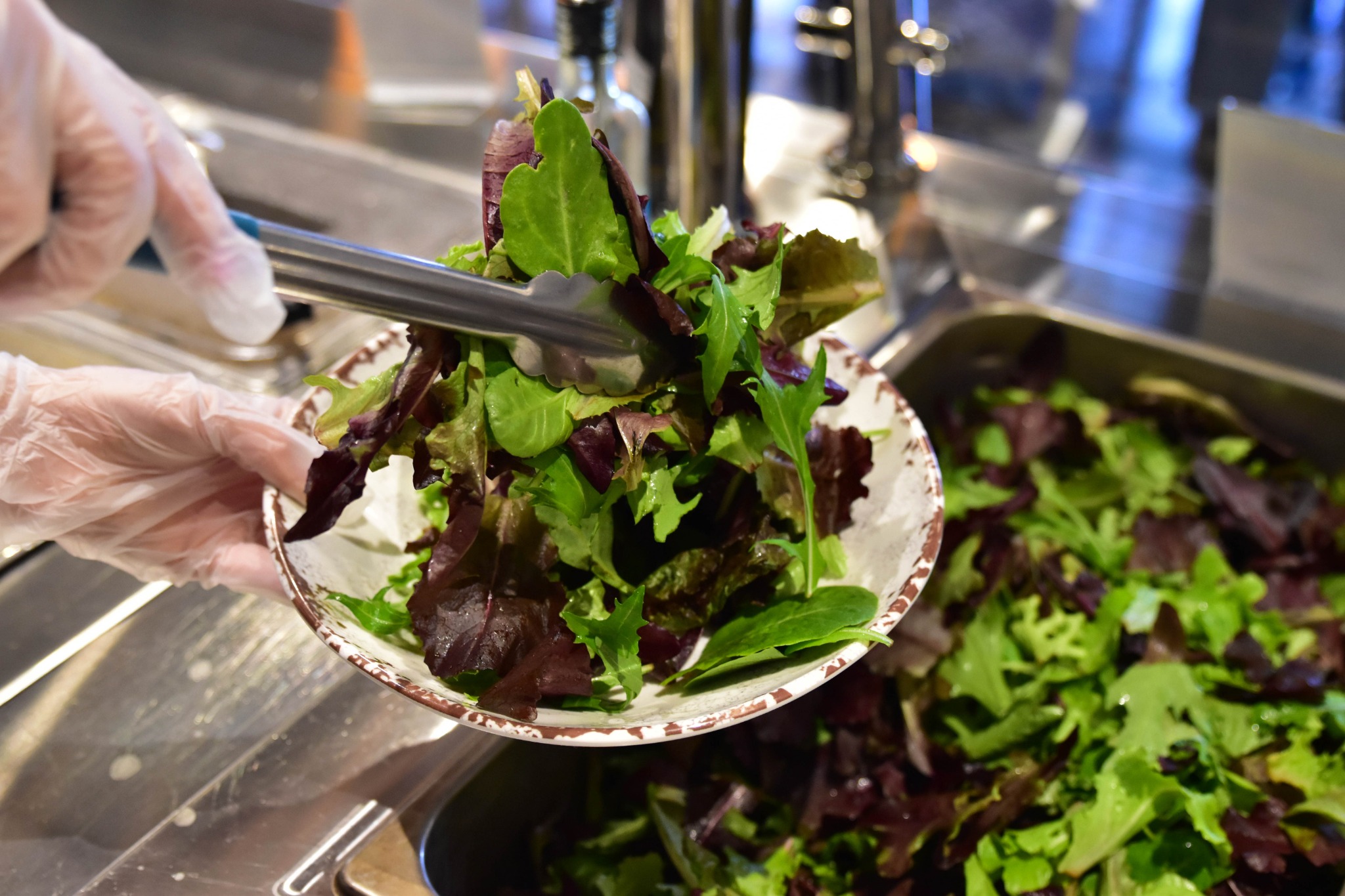 Fresh greens being added to a MezzeMe plate